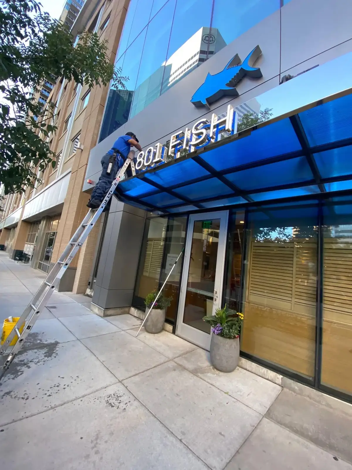Joe's Window Cleaning technician on a ladder cleaning storefront signage glass at a commercial building