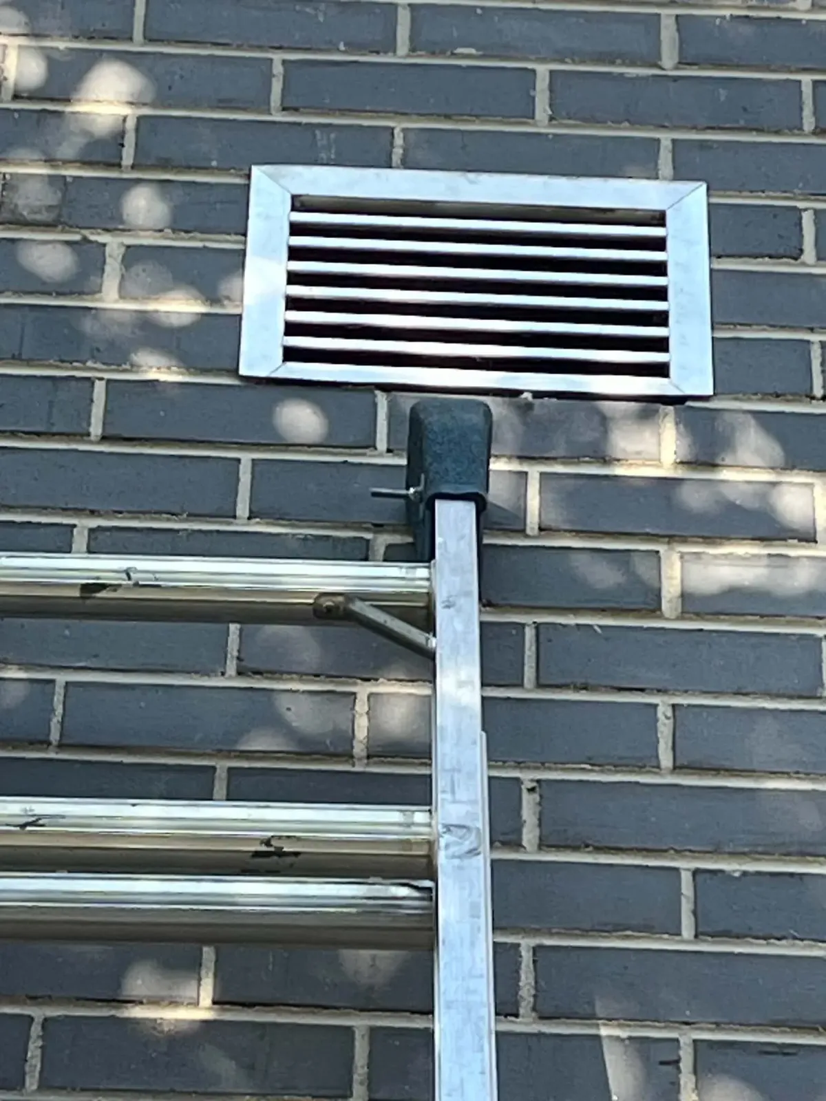 Close-up of a dryer vent cover on a brick wall, accessed from a ladder