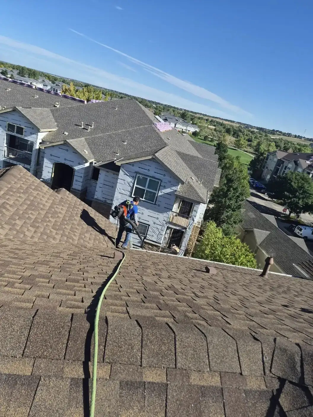 Joe's Window Cleaning technician using a blower to clear gutters on a steep multi-story roof