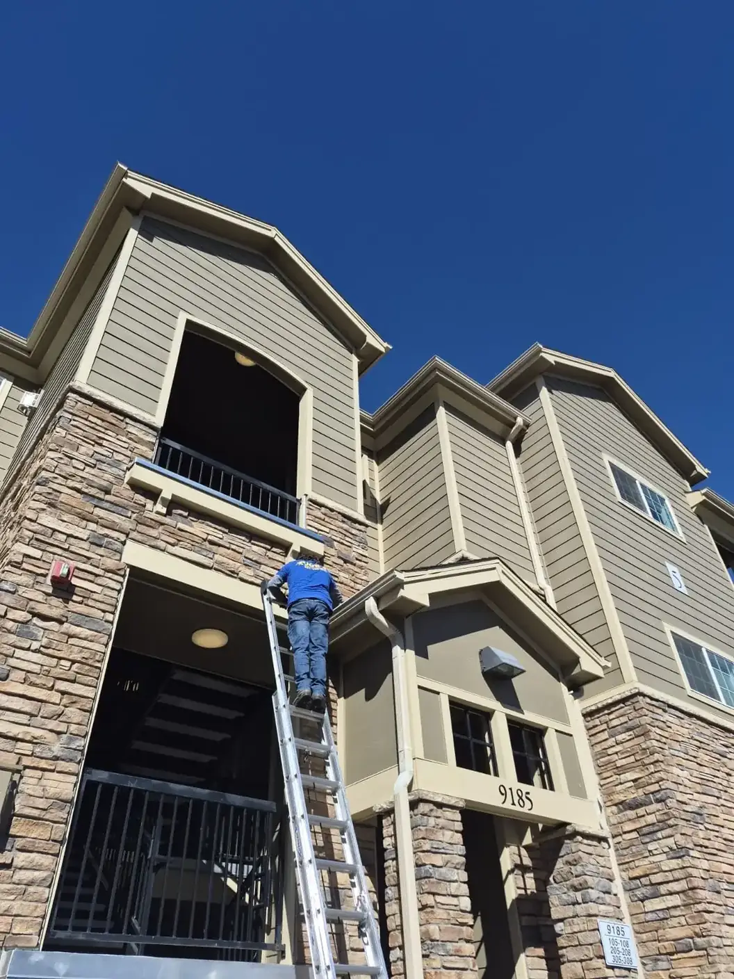 Joe's Window Cleaning technician on a ladder cleaning a multi-story apartment building's gutters