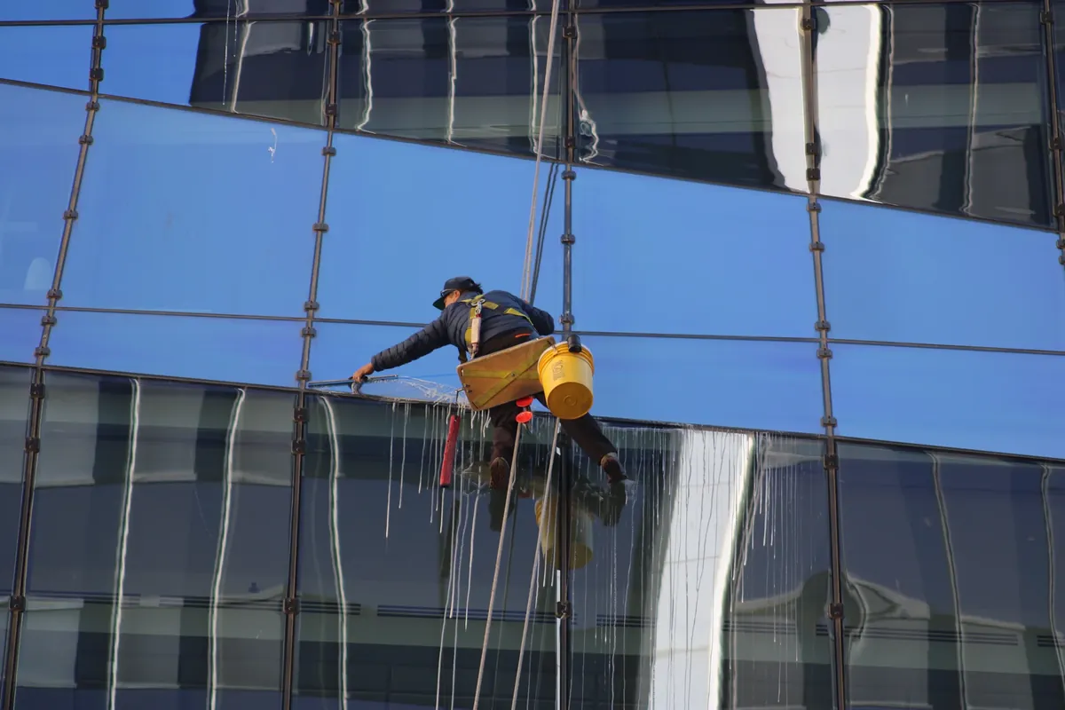 Joe's Window Cleaning technician on rope access squeegeeing a high-rise glass curtain wall