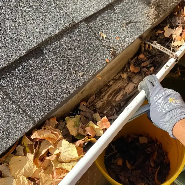 Gloved hand clearing leaves and debris from a residential gutter