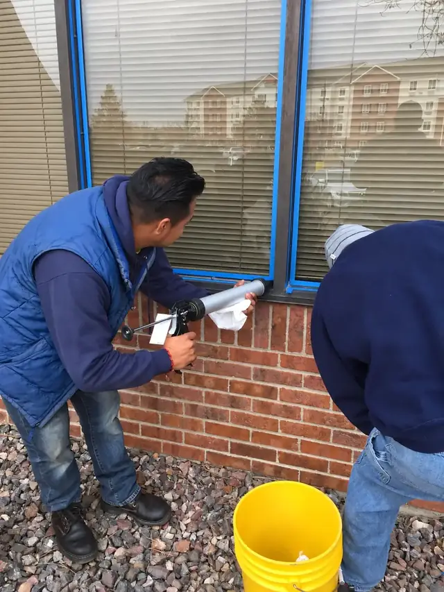 Joe's Window Cleaning technicians applying caulk to a commercial building window