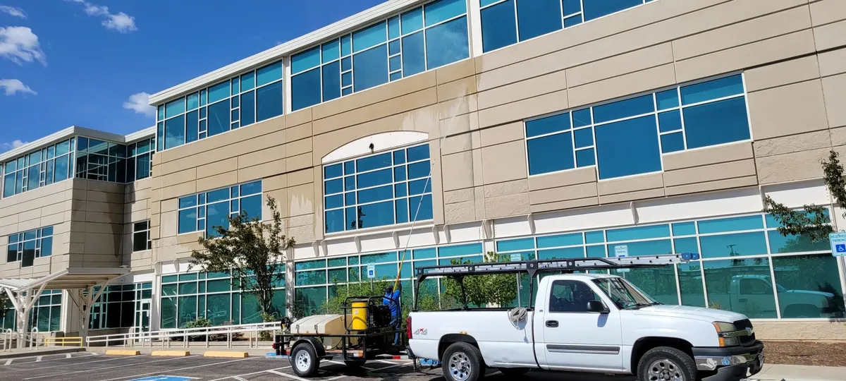 Joe's Window Cleaning technician pressure washing a commercial building's exterior, showing a clear line between cleaned and dirty siding