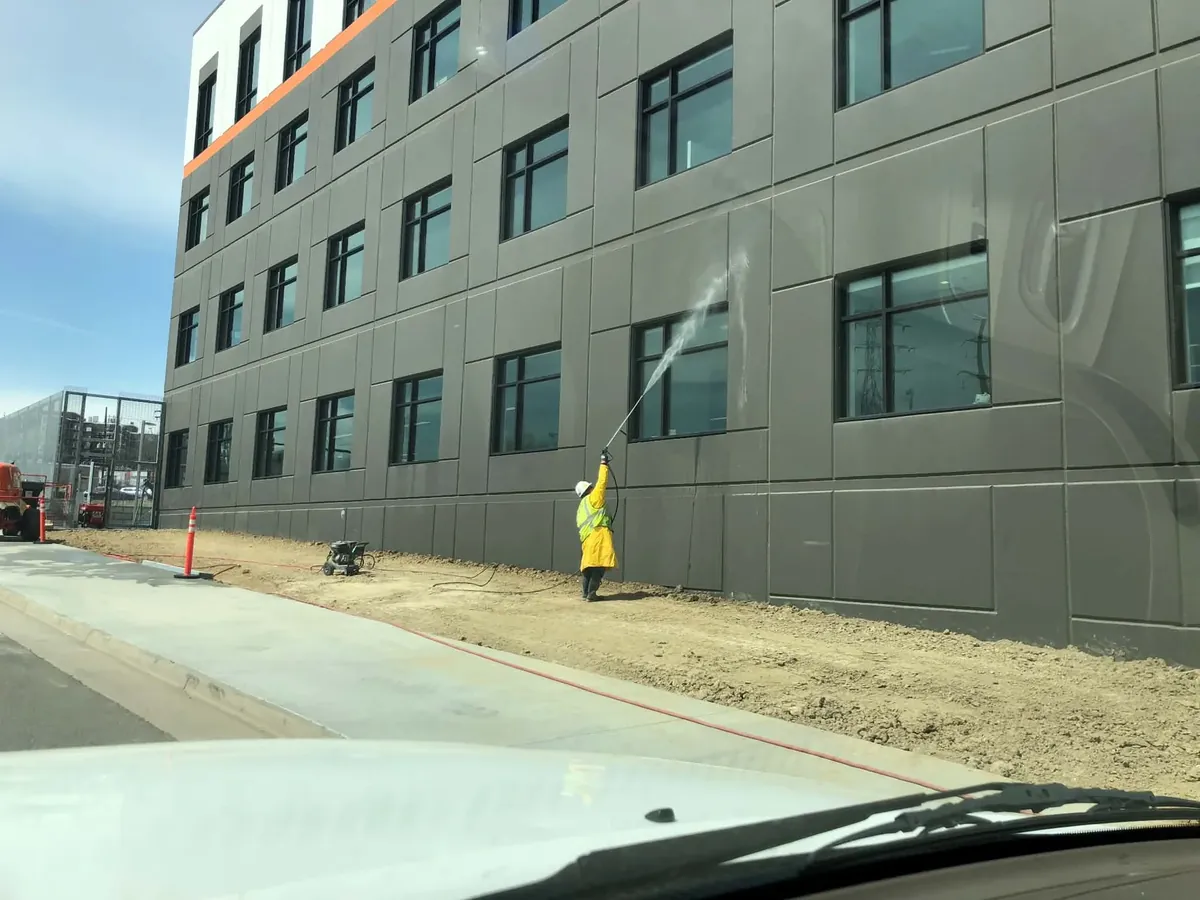 Joe's Window Cleaning technician pressure washing a commercial building's exterior