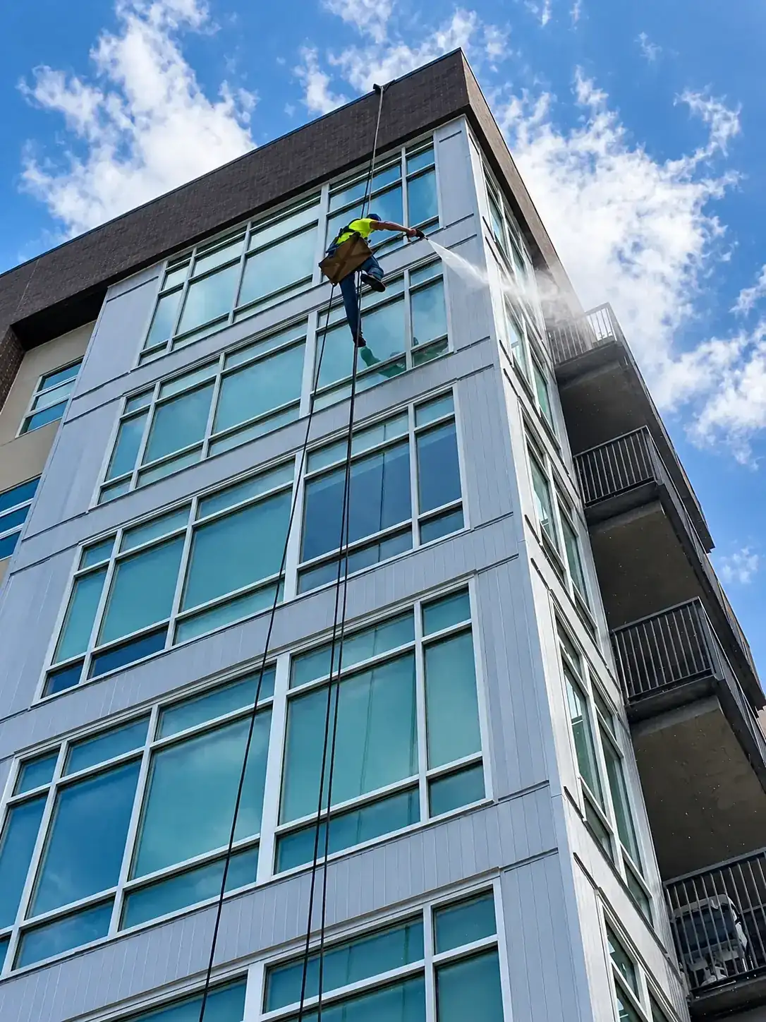Joe's Window Cleaning technician on rope access pressure washing a high-rise building facade