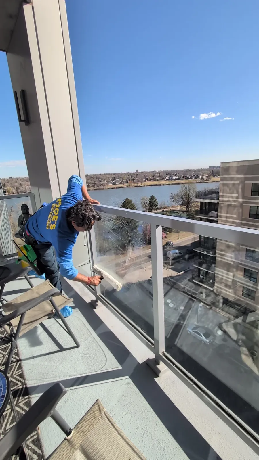 Joe's Window Cleaning technician cleaning a glass balcony railing overlooking the water