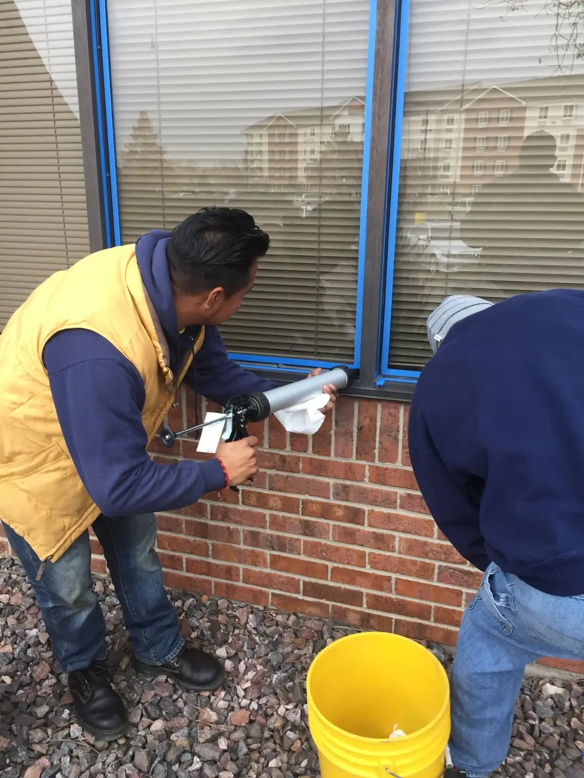 Joe's Window Cleaning technicians applying caulk to a commercial building window