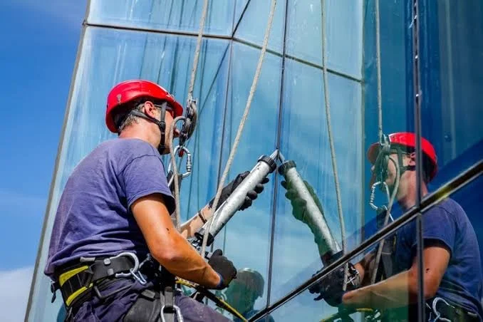 Joe's Window Cleaning technician on rope access applying caulk to a glass curtain wall