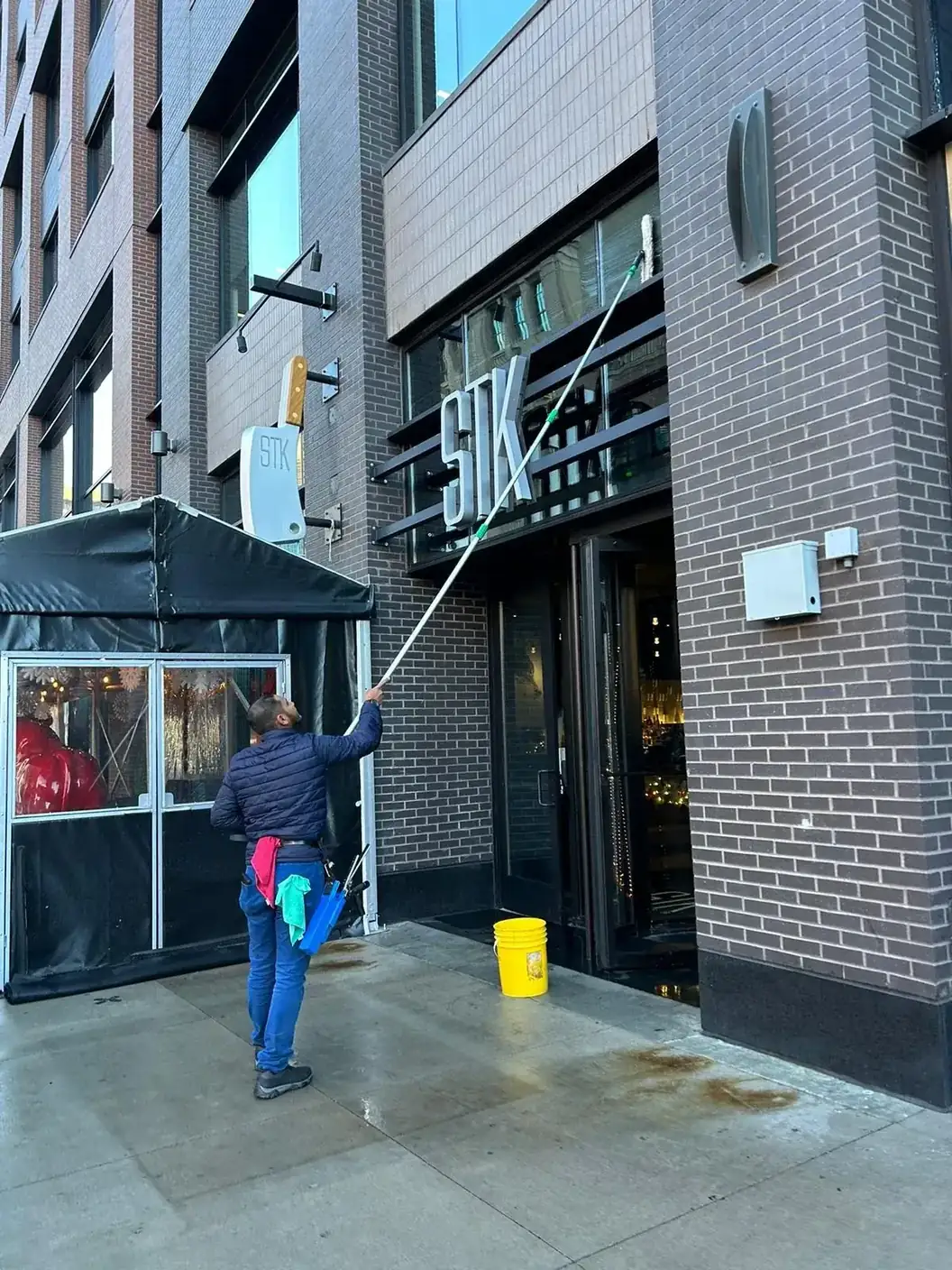 Joe's technician using an extension pole to clean the glass entrance of a downtown restaurant