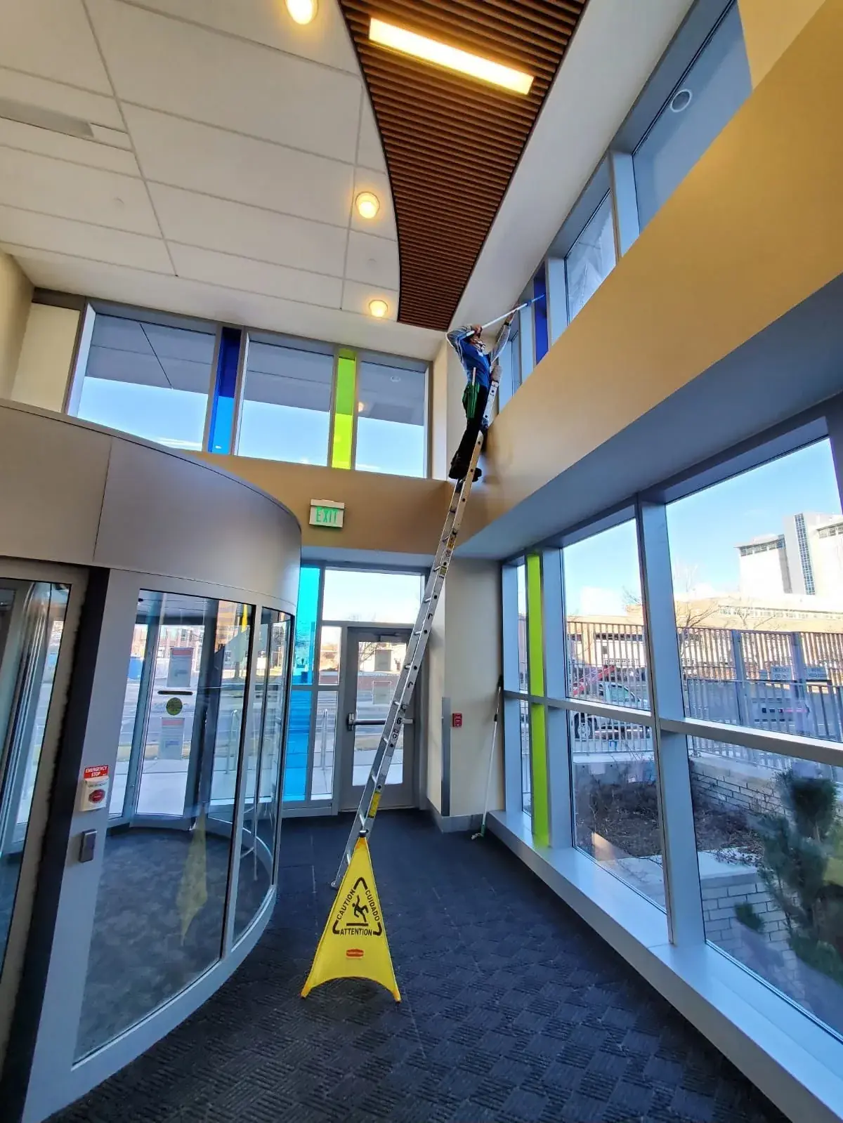 Joe's technician on a ladder cleaning the high windows of a building lobby