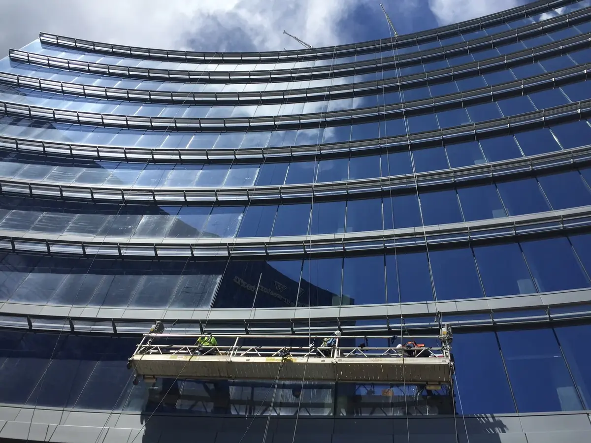 Joe's Window Cleaning crew on a swing-stage platform cleaning the curved glass facade of a high-rise building
