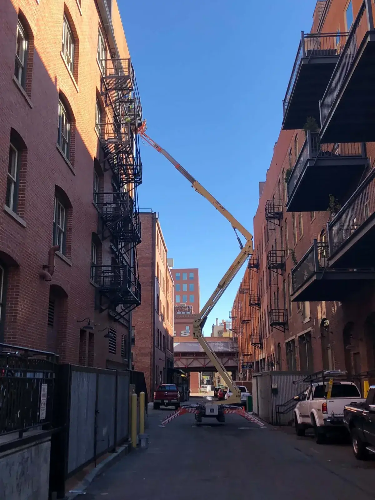 Boom lift reaching up a narrow brick alley to clean upper-floor windows