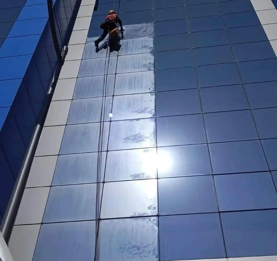 Rope access technician cleaning a mirrored glass facade, half of it already streak-free