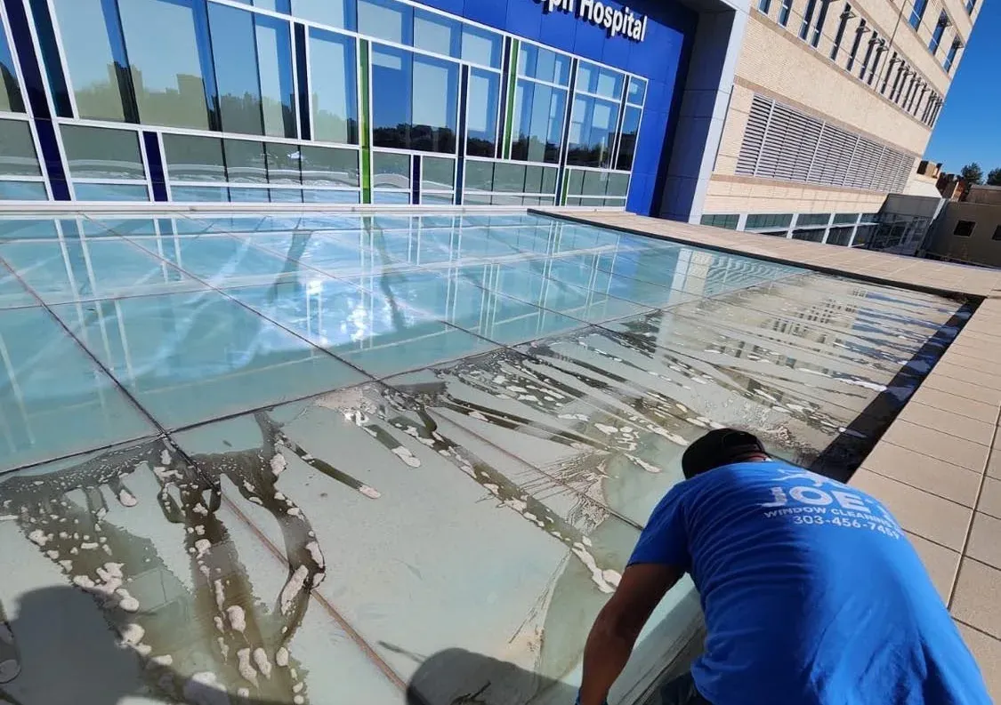 Joe's Window Cleaning technician removing heavy mineral buildup from a hospital glass canopy