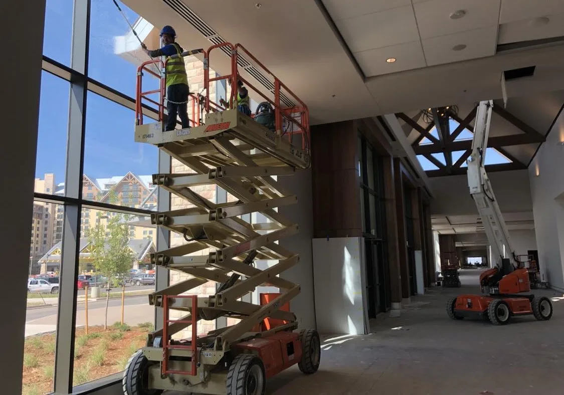 Joe's Window Cleaning technician on a scissor lift cleaning windows inside a building under construction