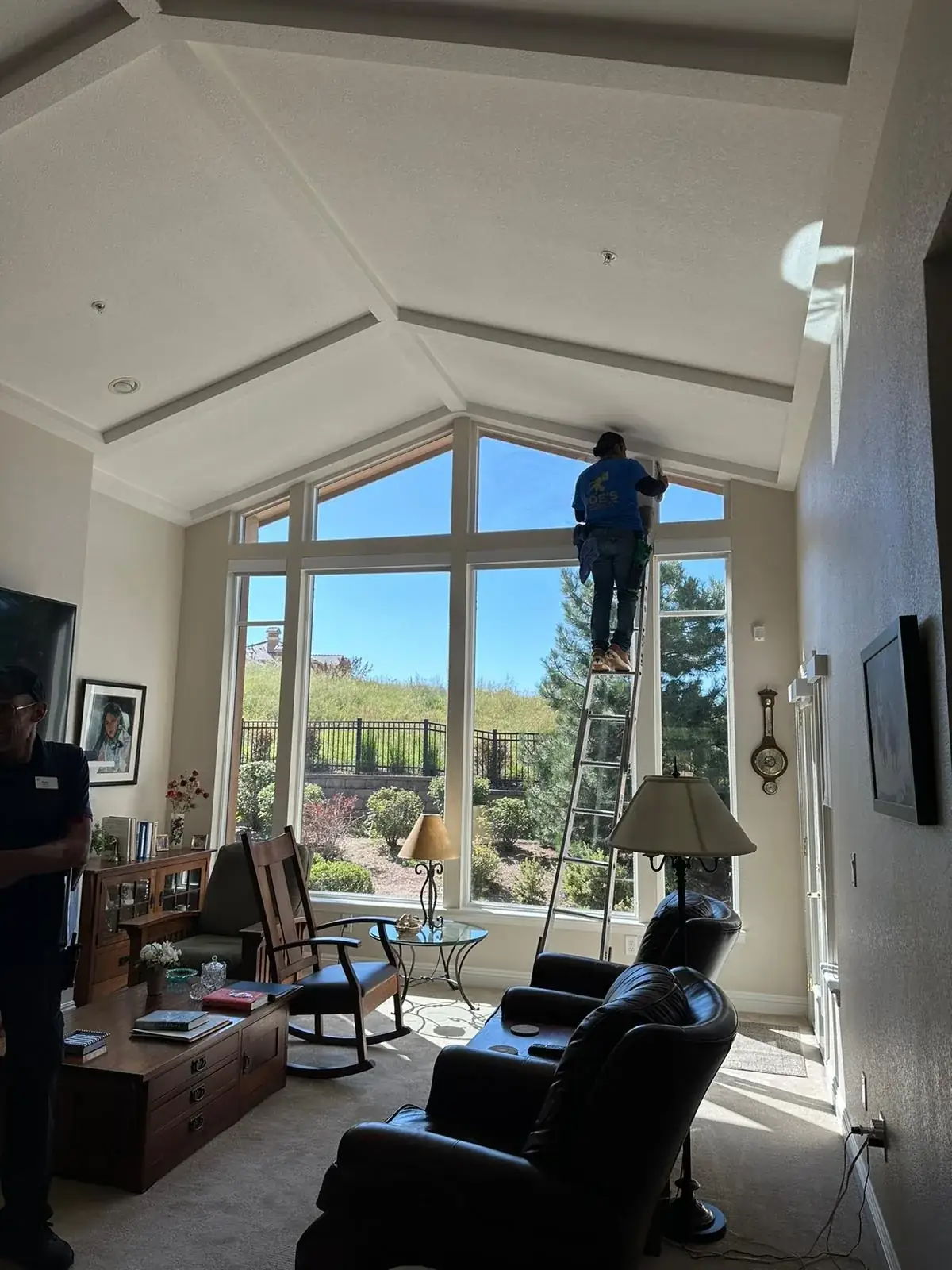 Joe's technician on a ladder cleaning tall windows in a vaulted living room