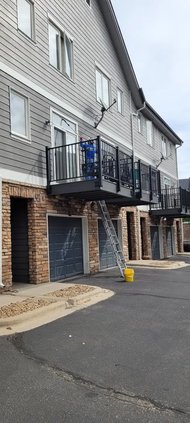 Joe's technician cleaning a townhome balcony window from a ladder