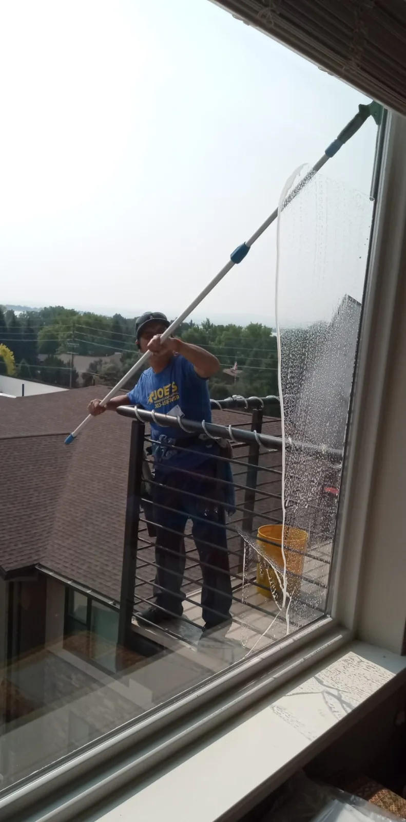 Joe's technician using an extension pole to clean windows from a balcony