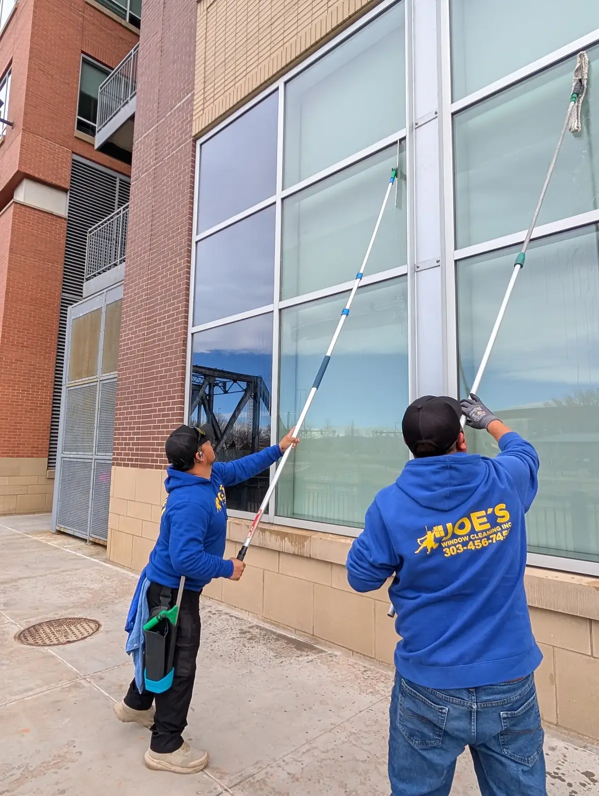 Two Joe's Window Cleaning technicians using extension poles to clean storefront windows on a commercial building