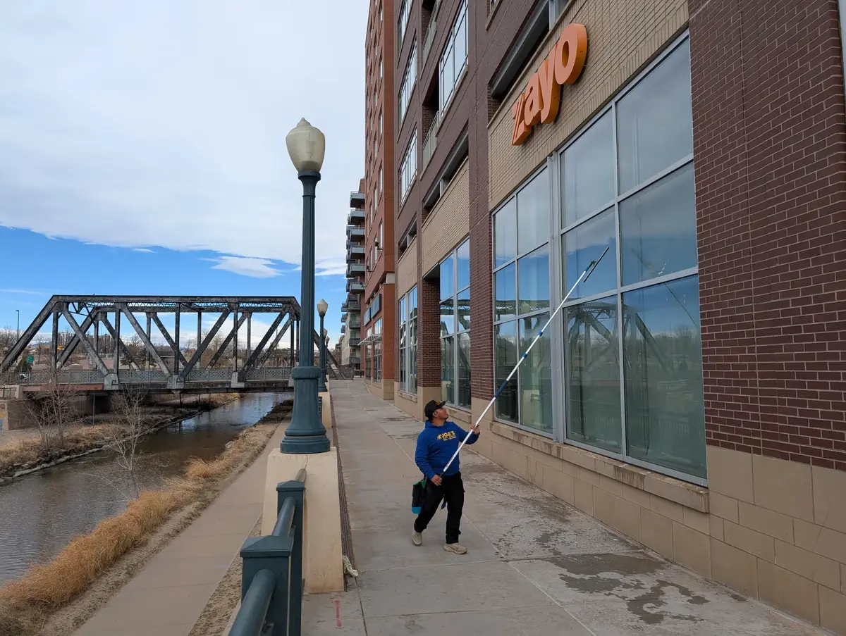 Joe's Window Cleaning technician using an extension pole to clean windows on a commercial office building