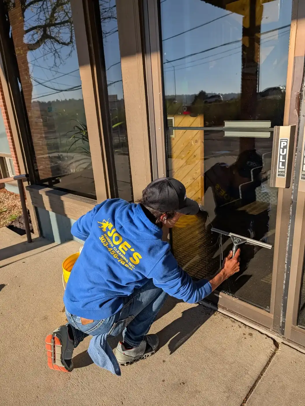 Joe's Window Cleaning technician squeegeeing a glass entrance door at a commercial storefront