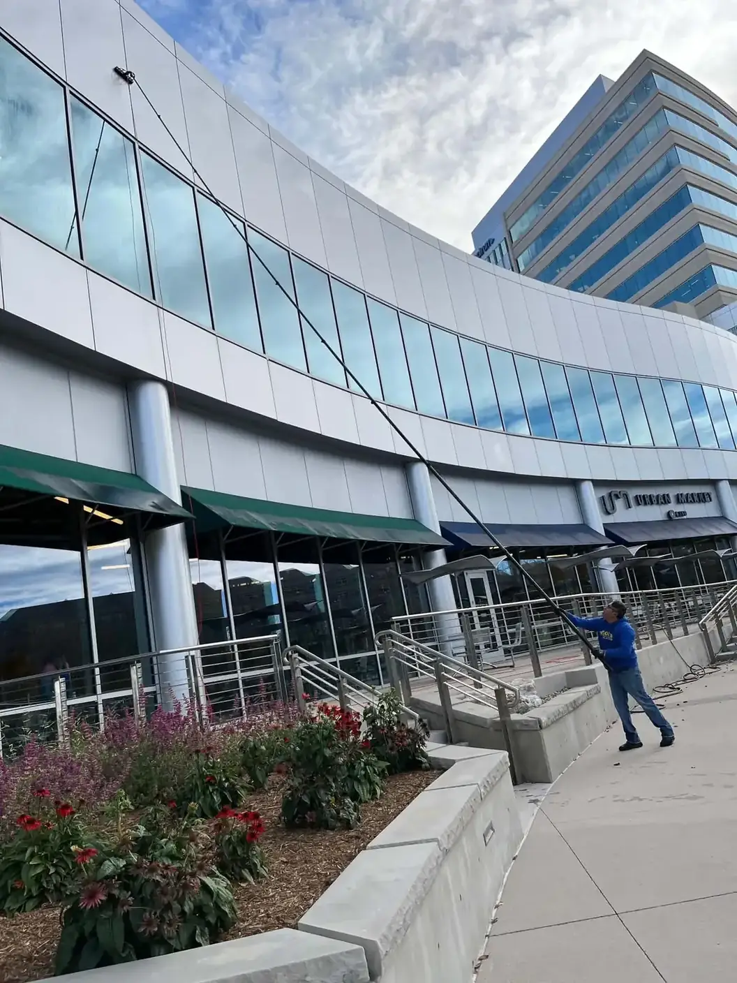 Joe's Window Cleaning technician using an extension pole to clean the curved glass exterior of a commercial building