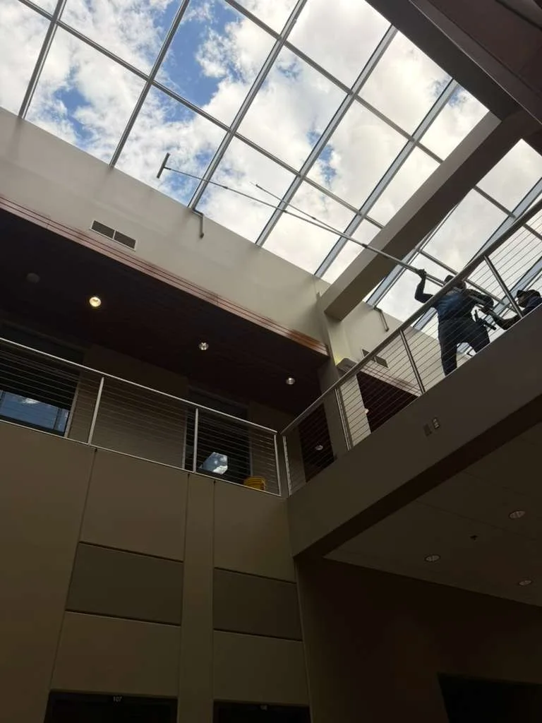 Joe's Window Cleaning technicians cleaning a glass atrium skylight from an interior walkway