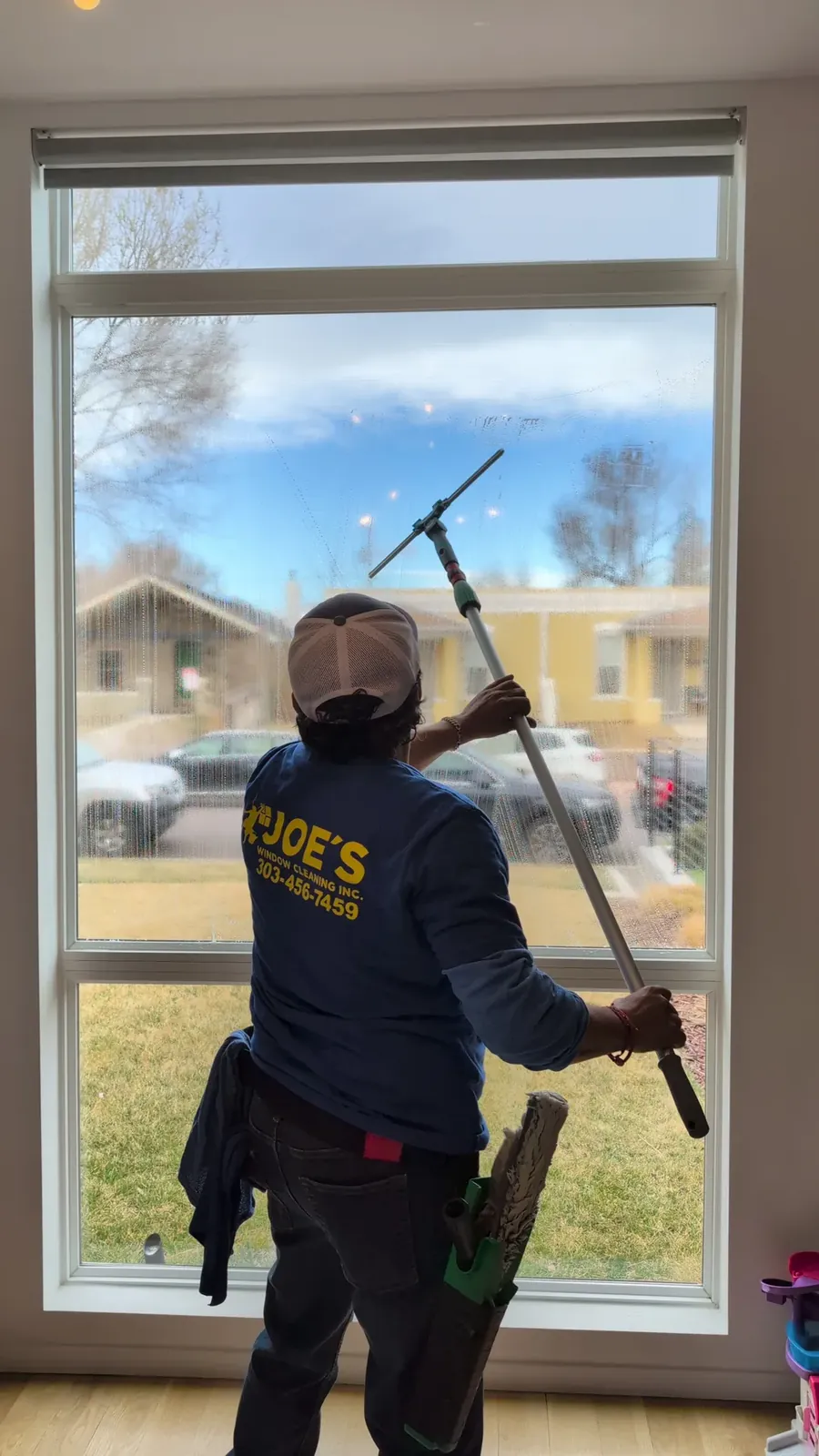 Joe's Window Cleaning technician cleaning an interior window overlooking a residential neighborhood